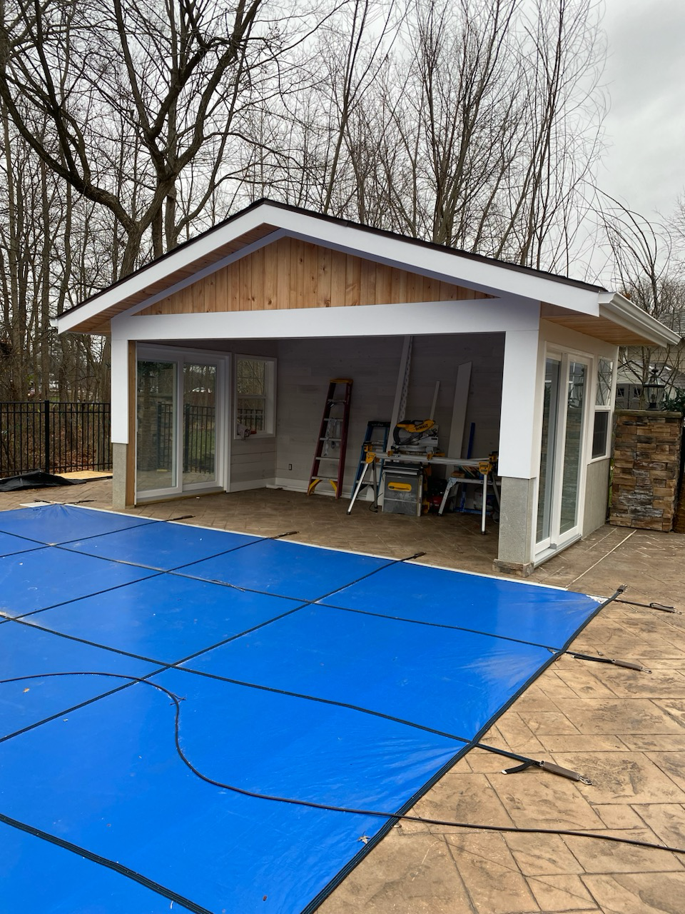 Covered outdoor pool house with cedar gable, sliding glass doors, and stamped concrete patio
