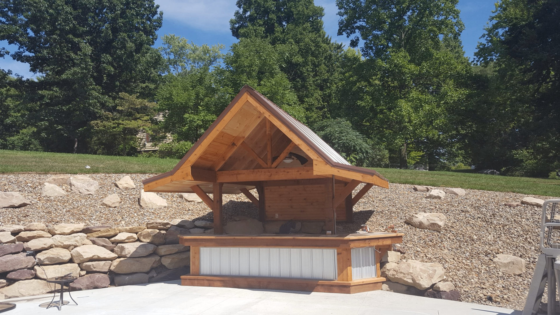 Custom cedar timber-frame poolside pavilion with metal roof and stone landscaping
