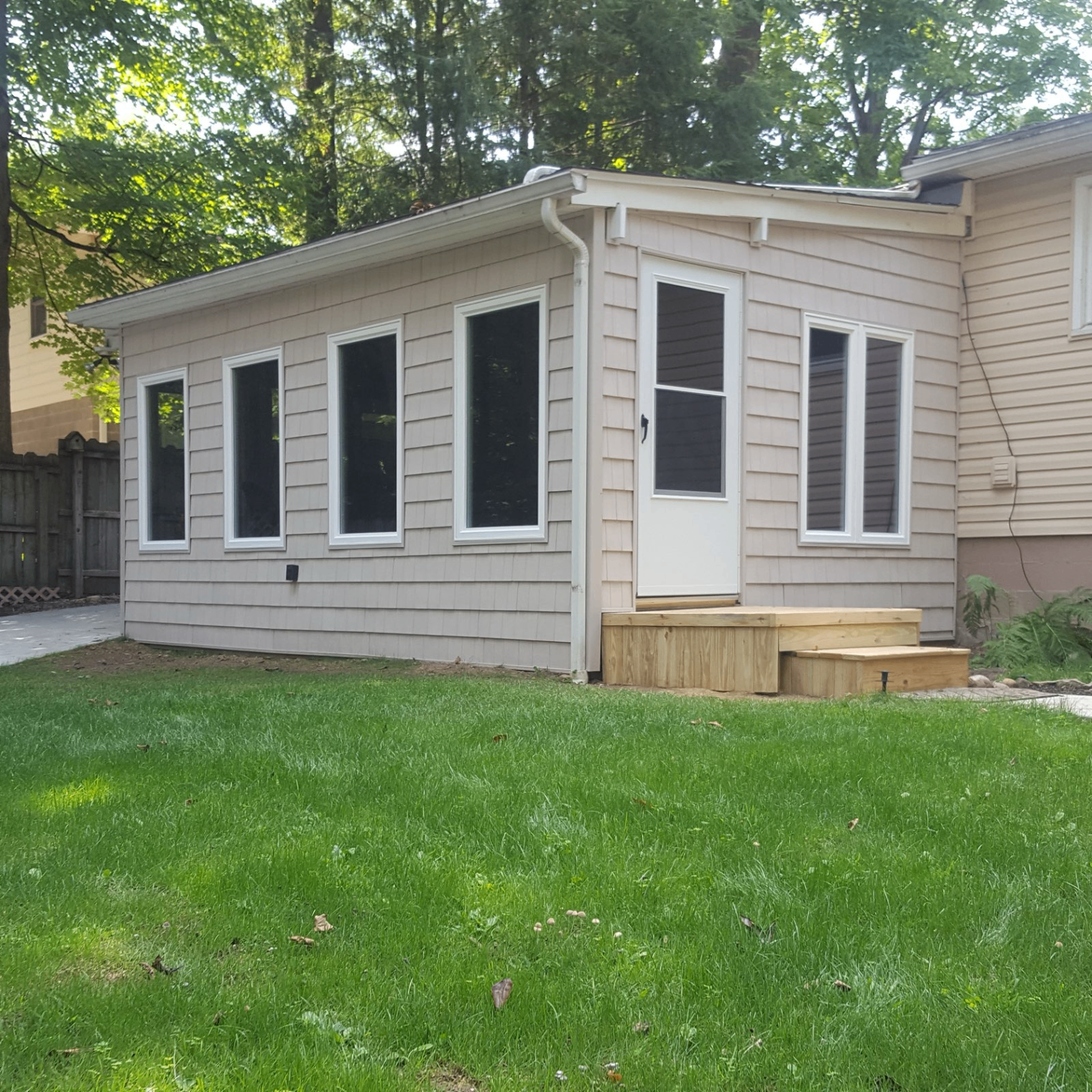 Home addition with tan shake siding, new windows, storm door, and seamless gutters